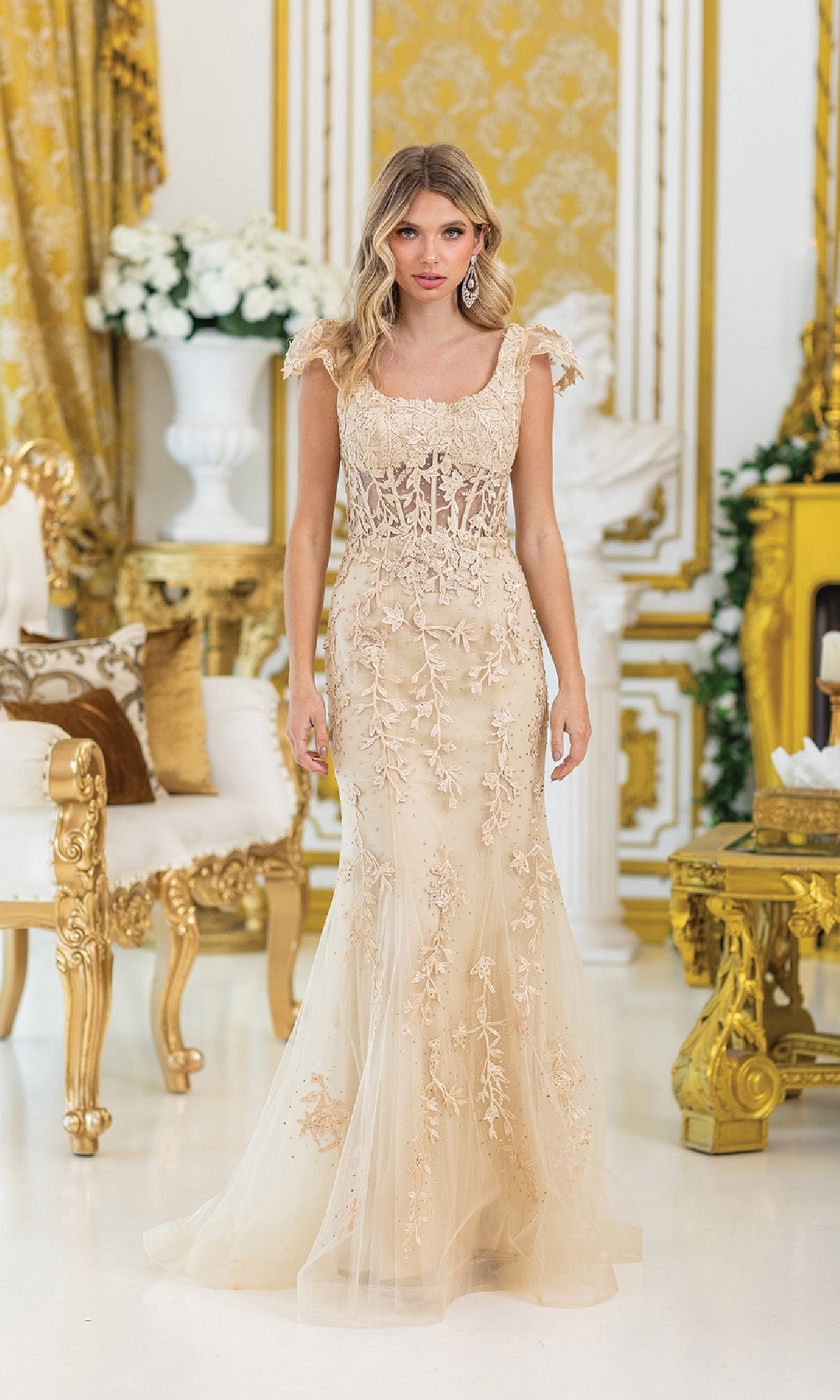 A woman in the Dancing Queen 4447 cap-sleeve long prom dress, featuring intricate embroidery, stands in an ornate gold and white room with floral arrangements and classic furniture.